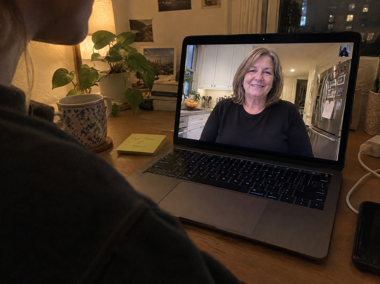 Over a daughter's shoulder: a video call with her mom, who is wearing the sweatshirt, and a sticky note that says Call Mom