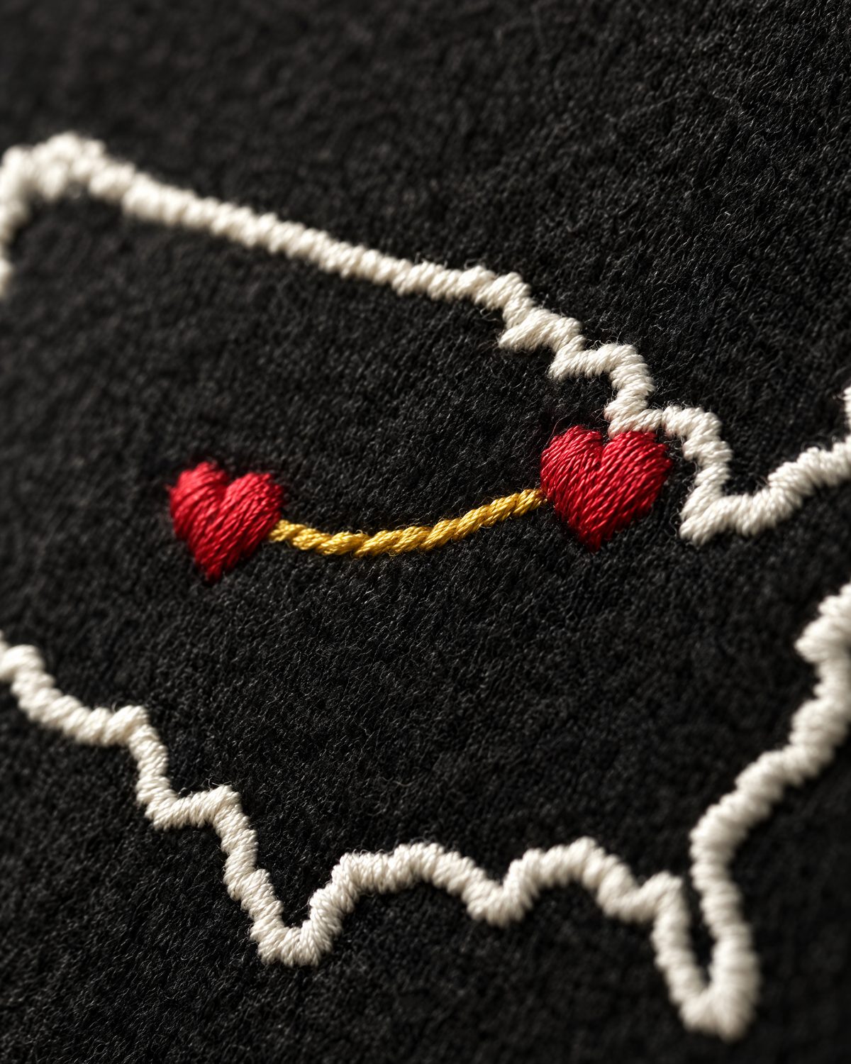 Close up: two red satin-stitched hearts and the gold thread between them on black fleece