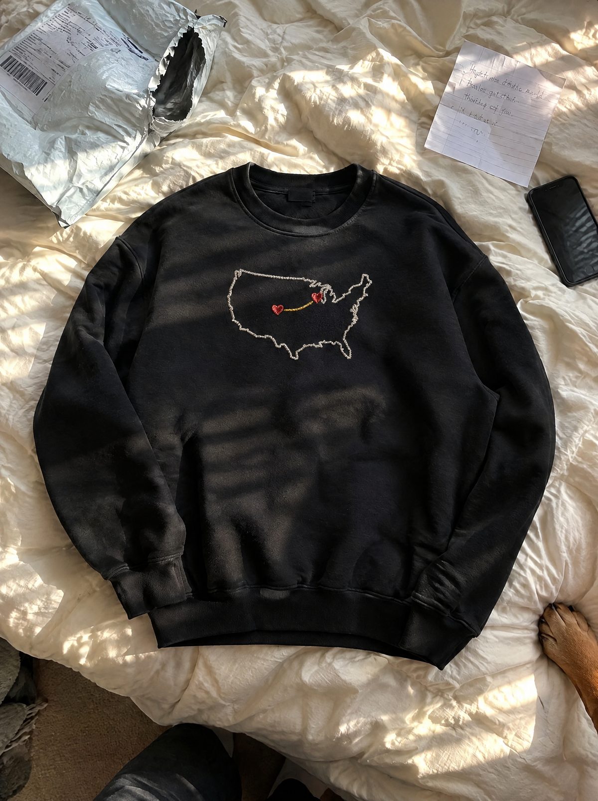 The sweatshirt just unpacked on a bed, the mailer torn open beside it