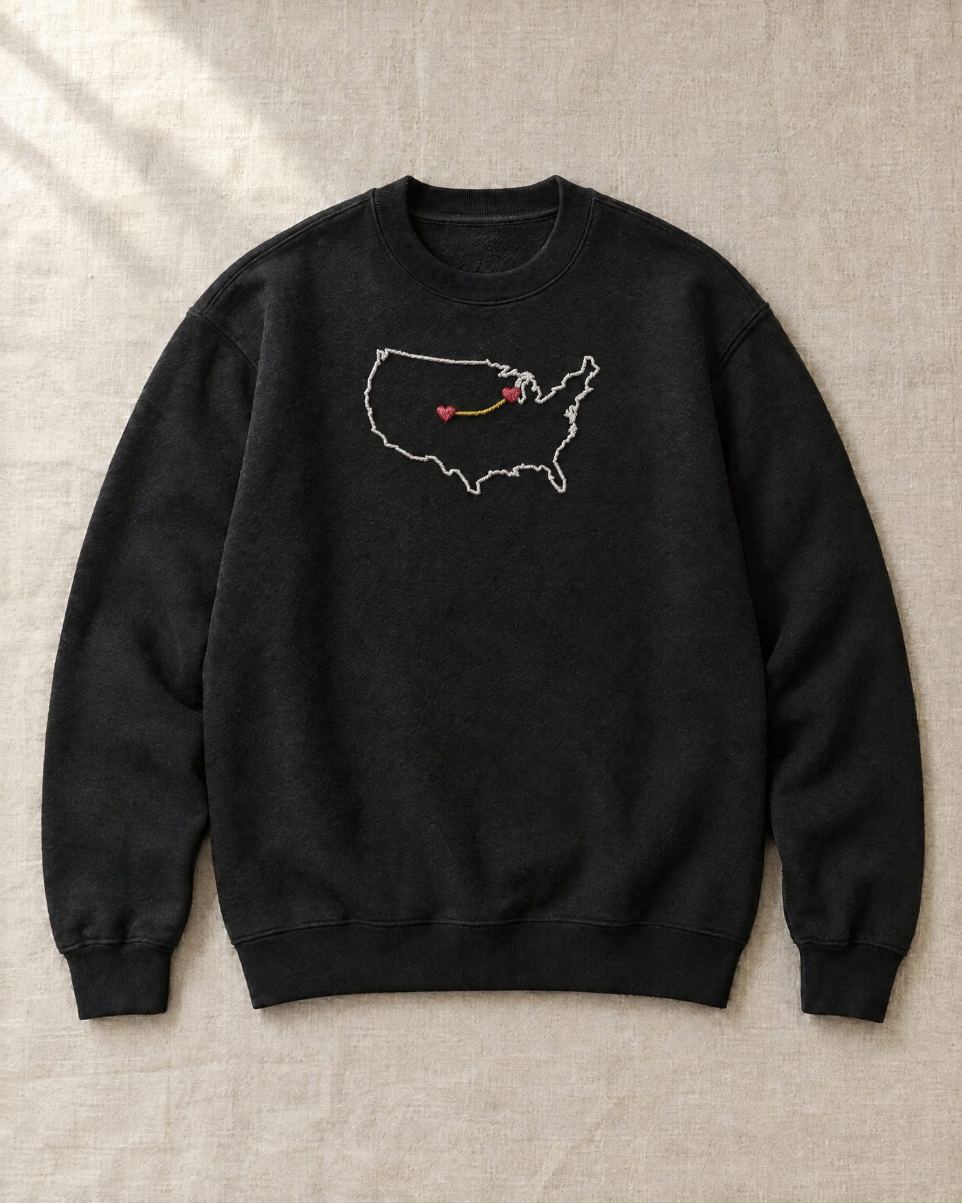 The sweatshirt laid flat on linen, the map embroidered across the chest